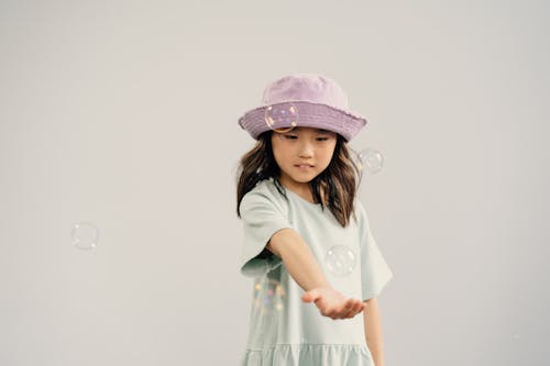 A Young Girl in Purple Hat Playing Bubbles