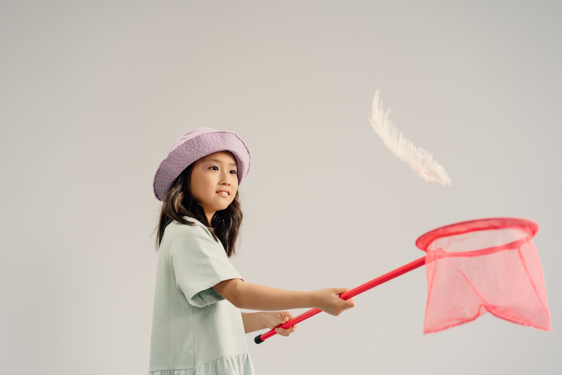 A young girl with a bucket hat and net playing indoors, featuring a white feather in mid-air.