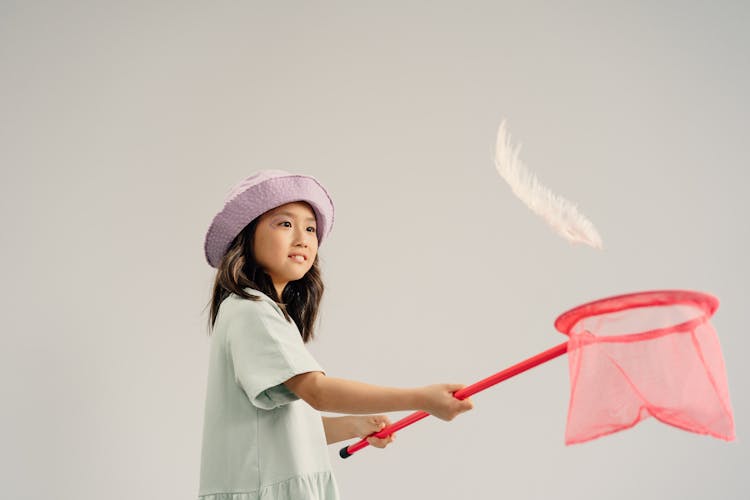 A Girl Catching A Feather Using A Butterfly Net