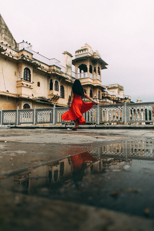 A Woman in Red Dress Walking Near Concrete Building