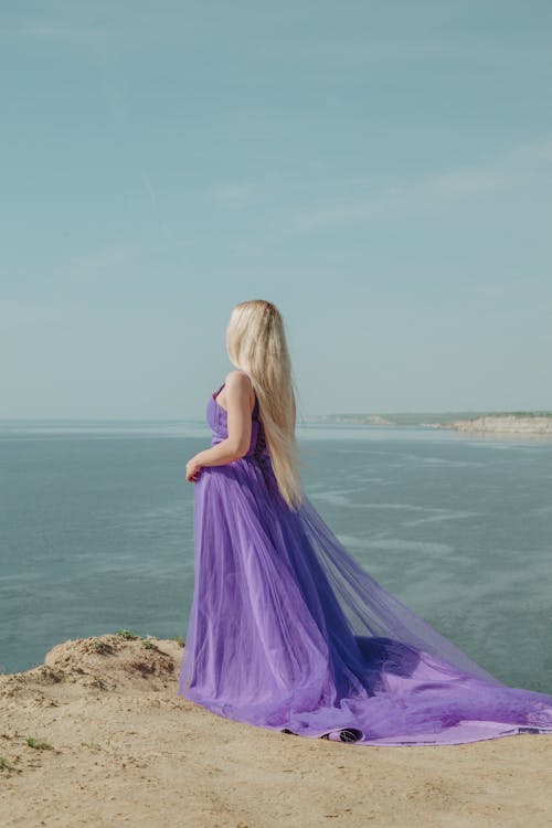 Anonymous elegant model in purple dress contemplating sea from mount