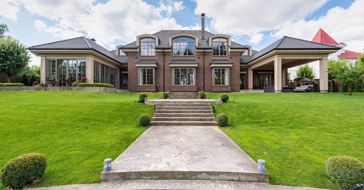 Elegant upscale mansion with lush green garden and clear blue sky.