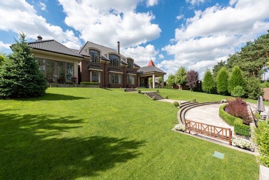 Elegant brick mansion with manicured lawn and garden under a bright blue sky.