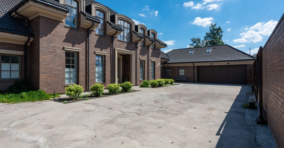 Elegant brick house exterior with a large driveway under a clear blue sky.