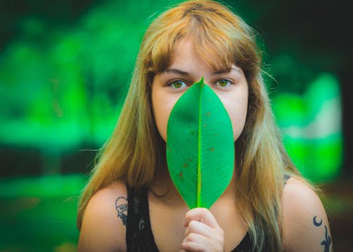 Женщина носить черный топ без рукавов, прикрывая рот, с помощью зеленого листа