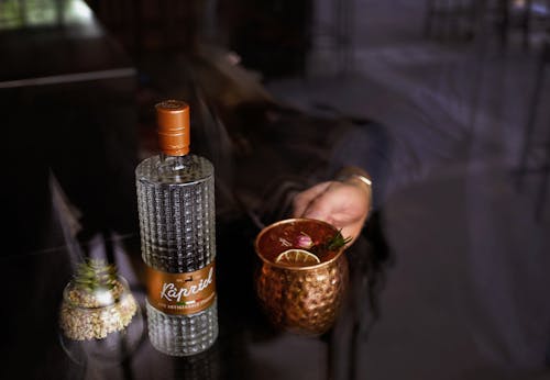 A Person Holding a Cup of Icy Cocktail Nar the Clear Glass Bottle