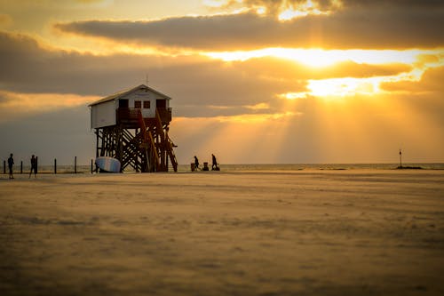 Kostenlos Weißes Rettungsschwimmerhaus Am Strand Unter Weißen Wolken Und Orange Himmel Genommen Stock-Foto