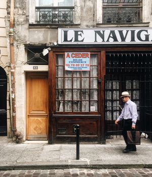 A businessman walks past a vintage shopfront in Paris, capturing urban life.