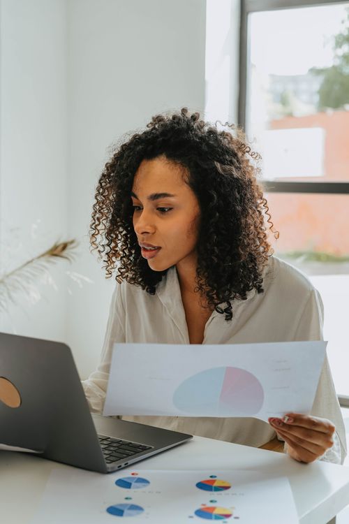 Free Confident woman working on a laptop, analyzing business charts in a bright office setting. Stock Photo