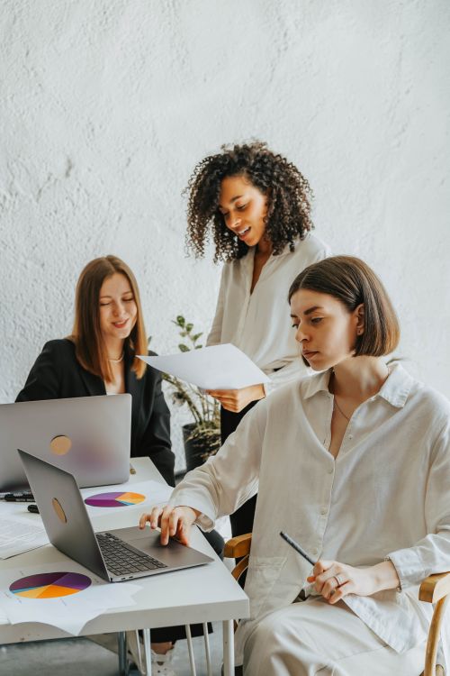 Free Three diverse businesswomen collaborating around laptops and documents in a modern office setting. Stock Photo