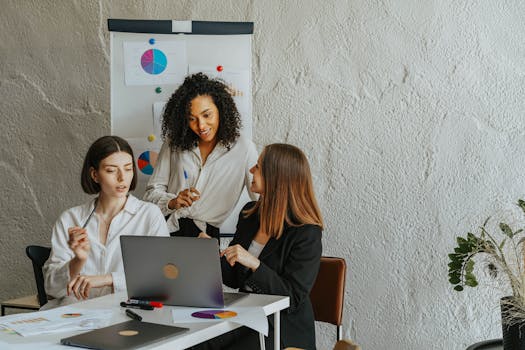 Three colleagues collaboratively working on a project in an office setting with charts and laptops.