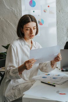 Young professional woman reviewing graphs at office desk with concentration.