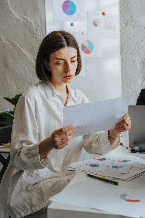 Free Young professional woman reviewing graphs at office desk with concentration. Stock Photo