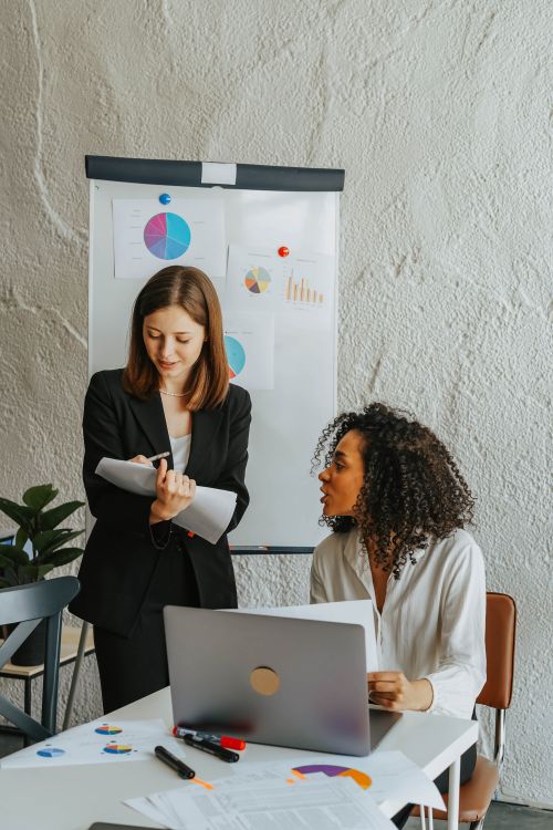 Free Two women collaborating in a modern office setting, focused on business analysis with charts. Stock Photo