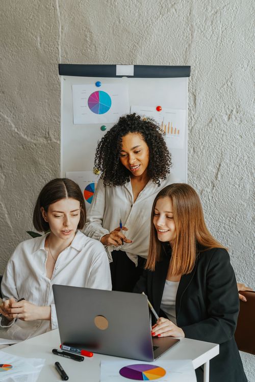 Free Three businesswomen work together on a laptop in a meeting room with charts. Stock Photo