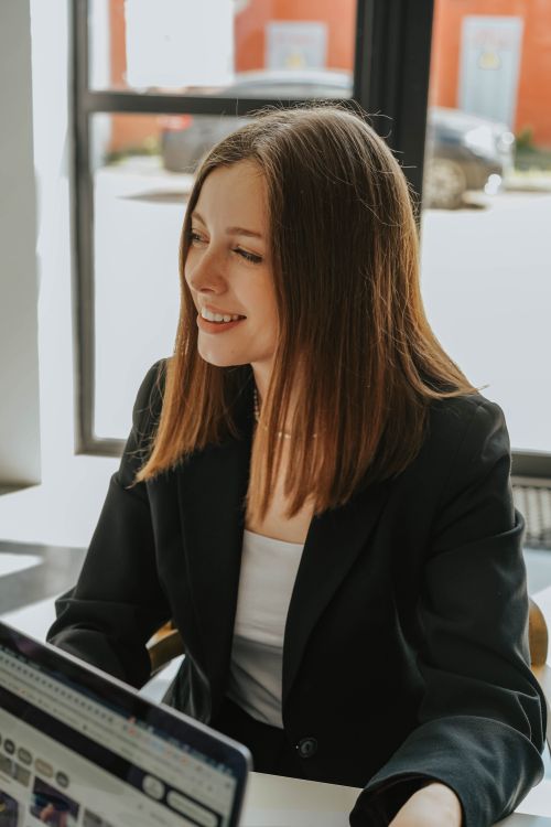 Free Young woman in formal attire smiling in a bright and modern office environment. Stock Photo