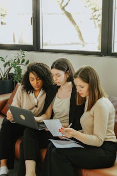 Three diverse businesswomen working together on a project in a modern office setting.