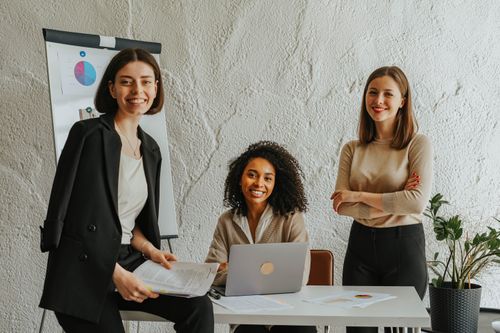 Free Three businesswomen meeting at a table, using a laptop and presenting charts in a modern office. Stock Photo