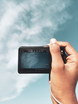 Close-up of a hand holding a digital camera, capturing a cloudy sky. Perfect for photography-themed content.