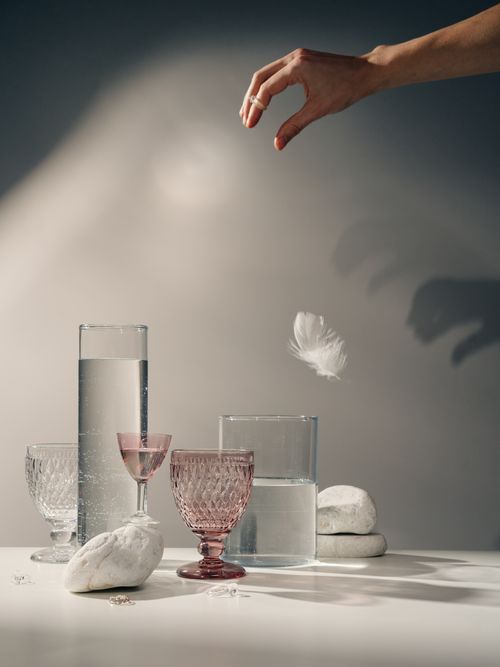 Free Artistic still life featuring crystal glasses, a feather, and a hand with shadows. Stock Photo