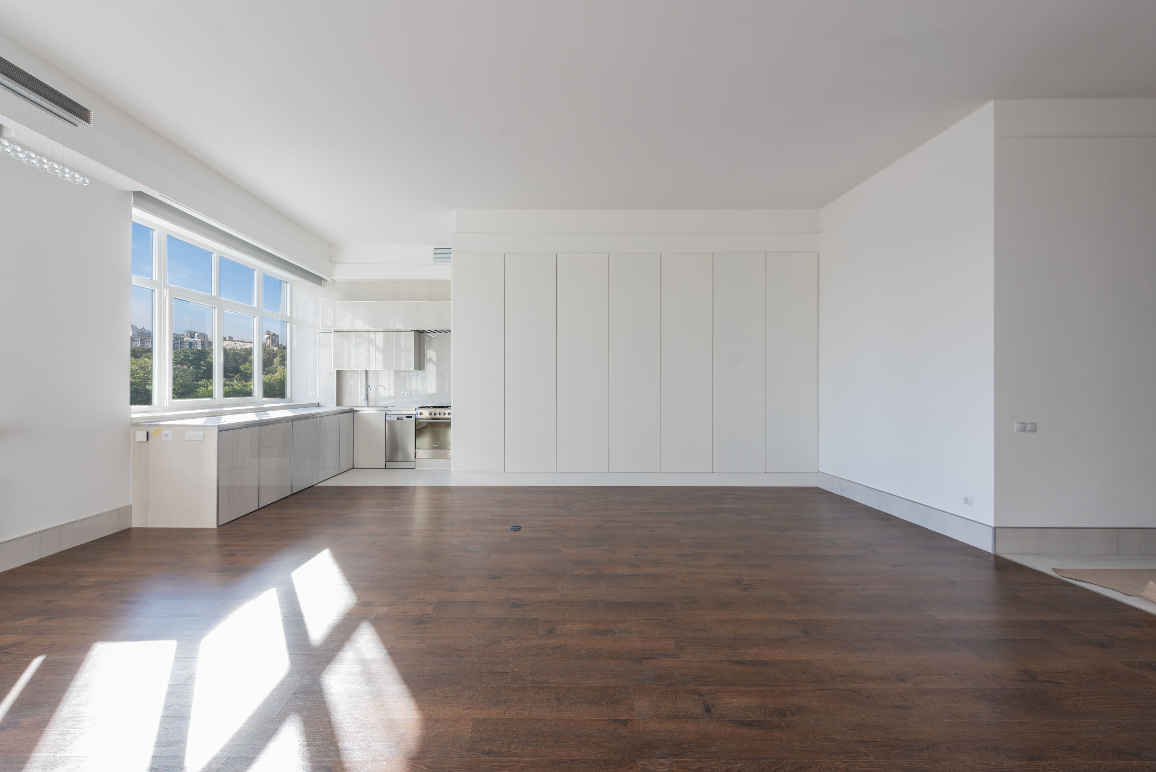 Pièce vide au parquet clair, kitchenette blanche encastrée, murs fraîchement nettoyés