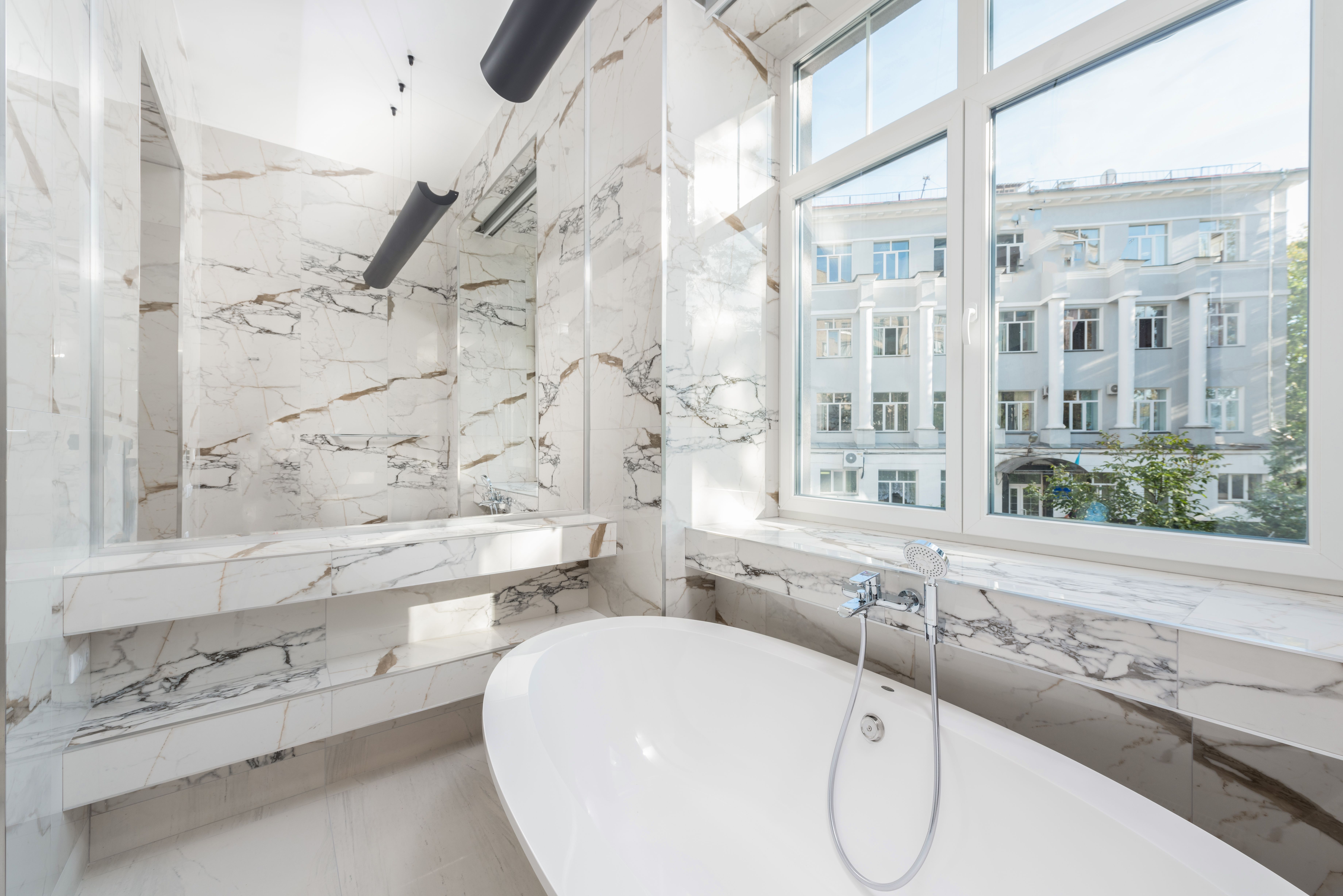 Elegant marble bathroom featuring a modern bathtub and a scenic city view. — Trójmiasto