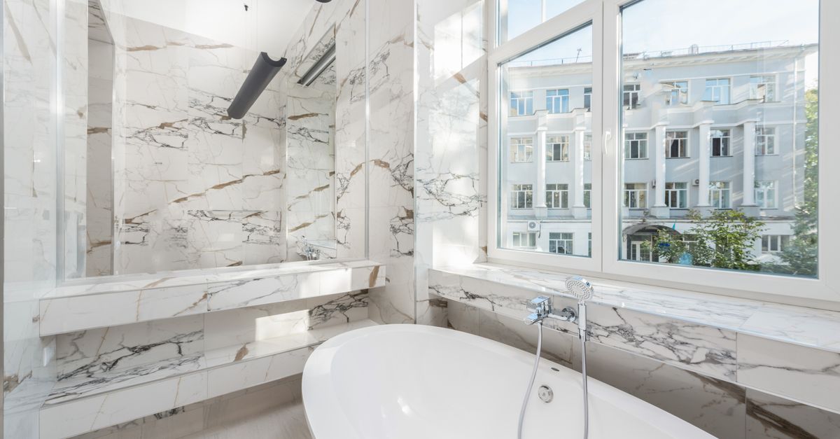 Elegant marble bathroom featuring a modern bathtub and a scenic city view.