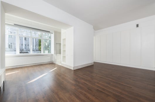 Bright empty room featuring large windows and wooden flooring.