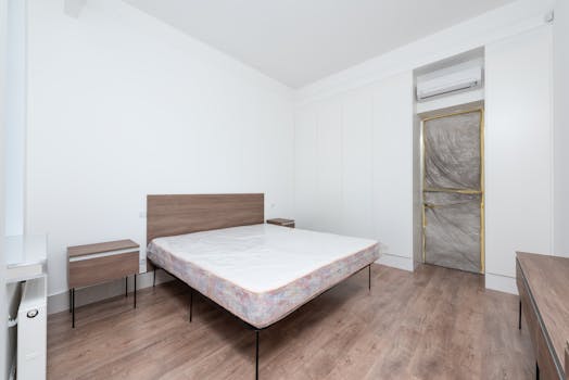 Spacious minimalist bedroom featuring a large bed, sleek furniture, and wooden flooring.