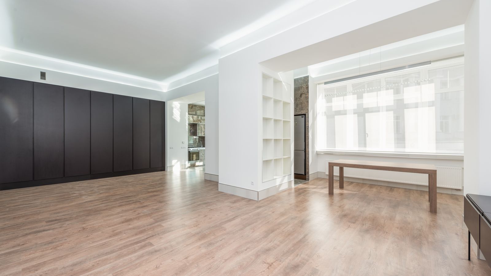 A spacious, minimally furnished room with light wood floors and white walls