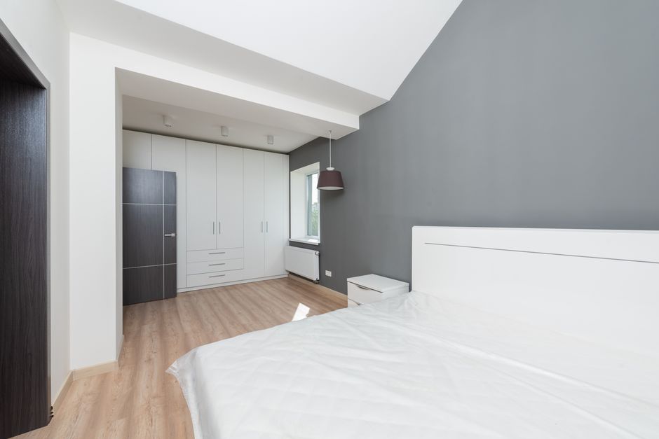 Spacious modern bedroom with a gray accent wall and minimalist design featuring wooden flooring.