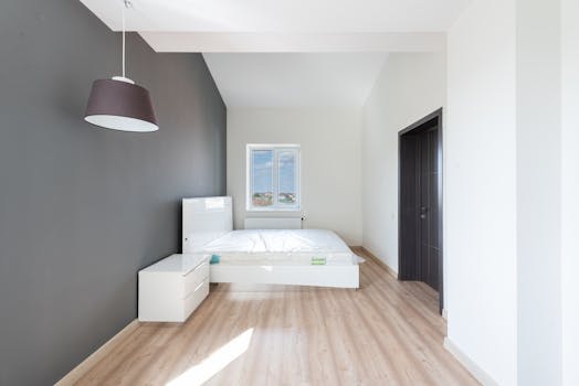 Bright and minimalist bedroom interior with wooden flooring and a large window.