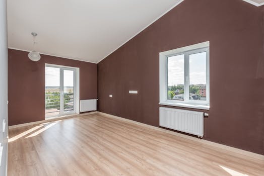 Bright and spacious beige room with brown walls, large windows, and a wooden floor.