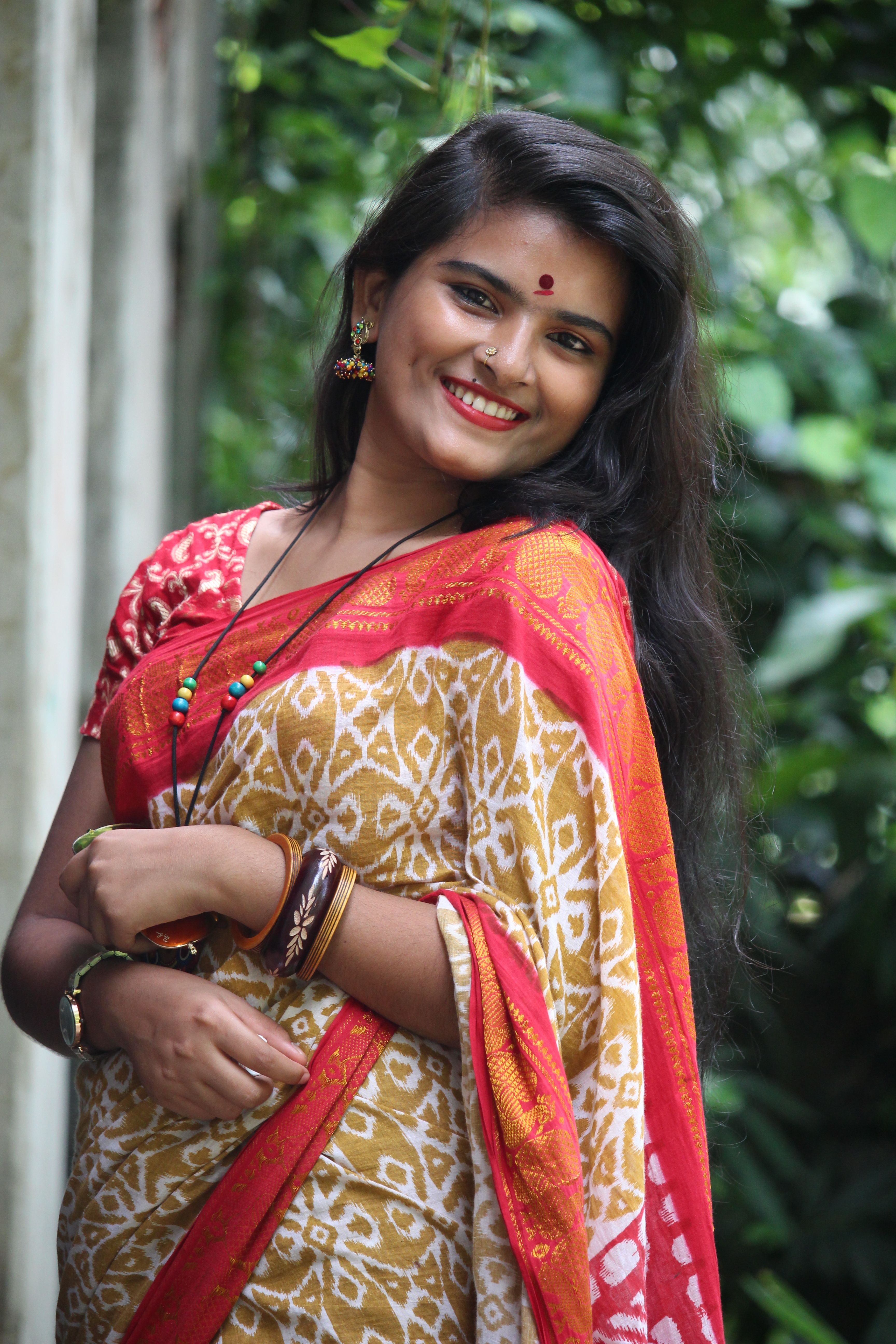 A smiling woman in a traditional saree, standing outdoors, exuding warmth and cultural richness.