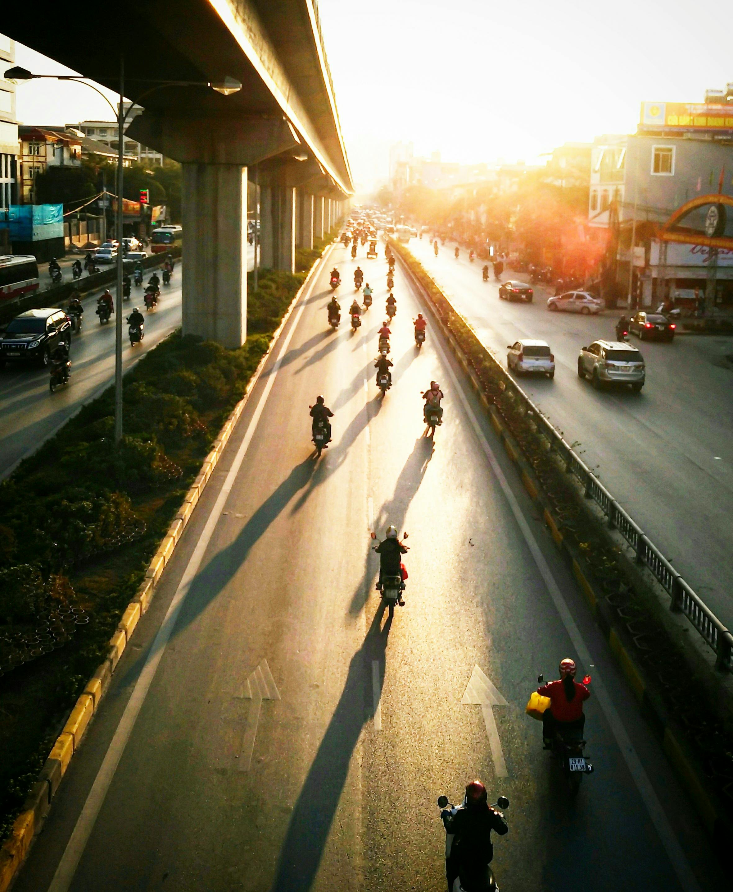 Vibrant scene of motorbikes under elevated tracks in Hanoi, Vietnam during sunset.