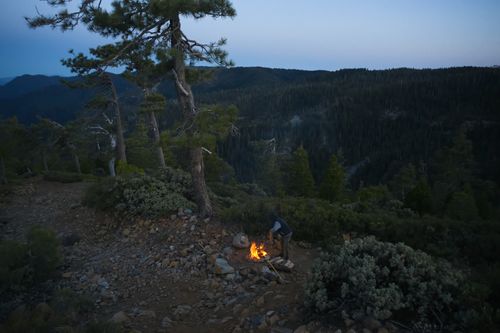 Free A lone camper starts a campfire surrounded by pine trees and rolling hills at dusk in Willow Creek, CA. Stock Photo