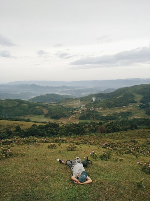 A Person Lying on Green Grass Field Under the Cloudy Sky