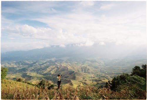 A Man Standing on Mountain while Taking Picture