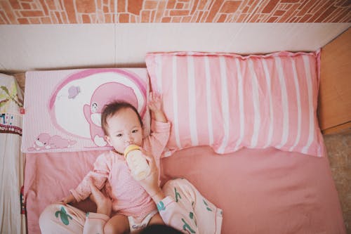 Free Person Holding and Milk Bottle Feeding a Baby Lying on Bed Stock Photo