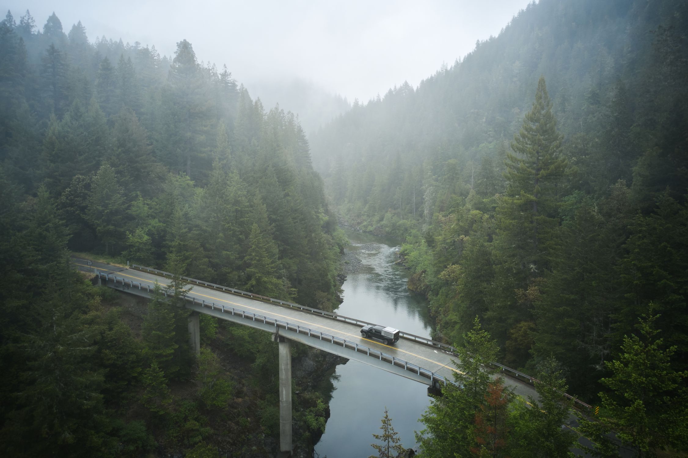 Aerial view of a foggy bridge over a river in a dense Redwoods forest near Crescent City, CA.