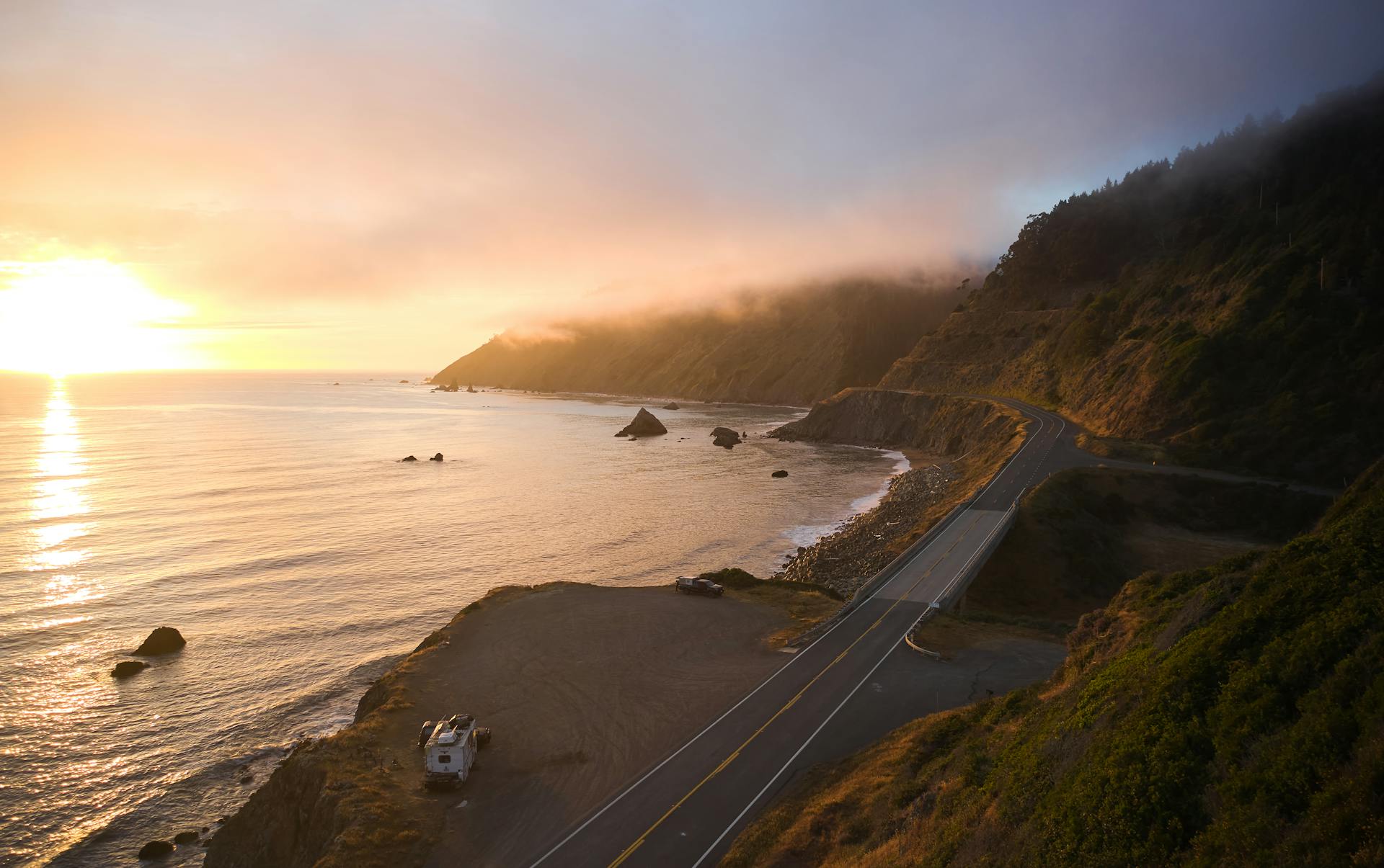 A stunning aerial view of the scenic California coastline at sunset with misty hills and a winding road.