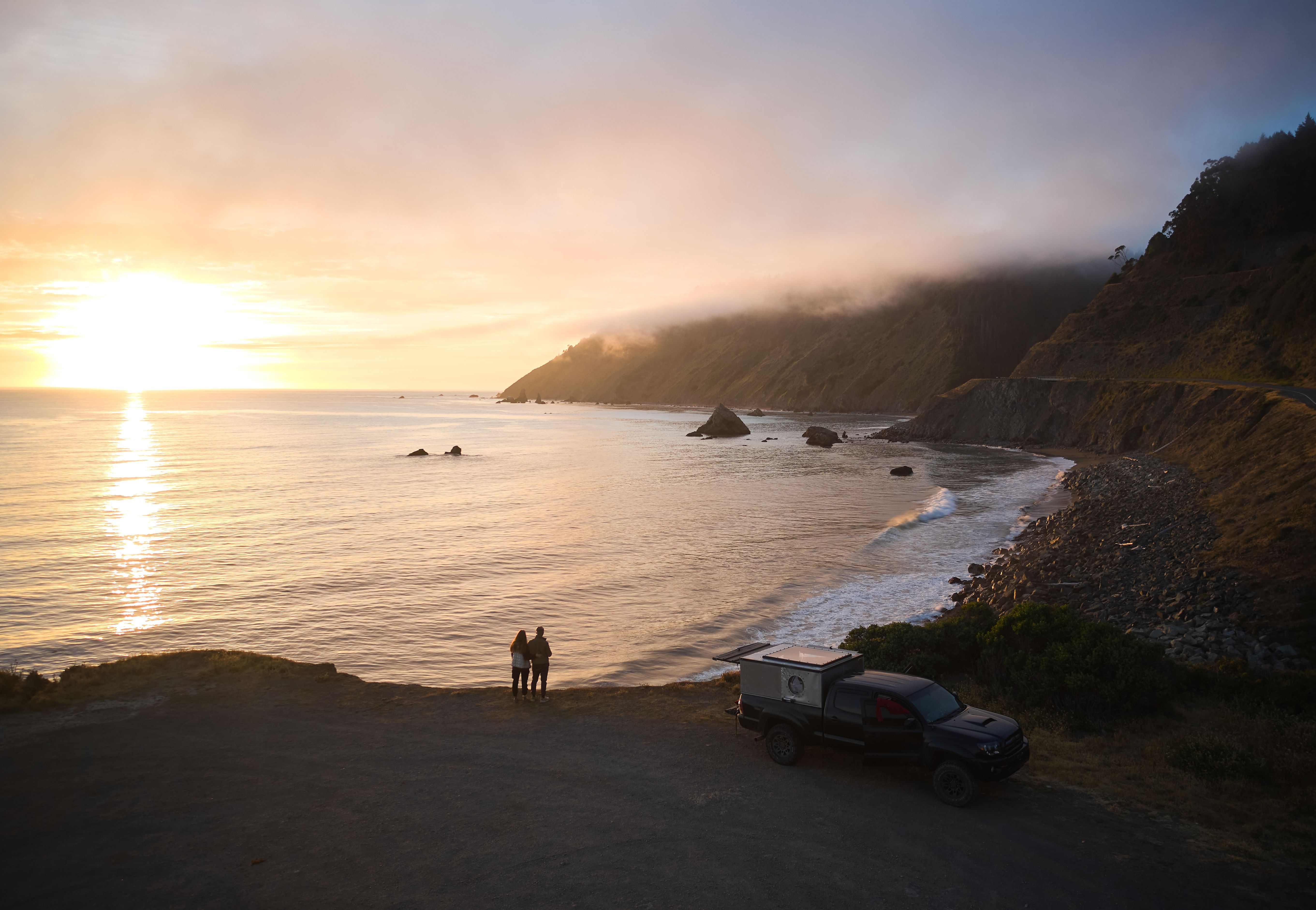Couple standing at the edge of the Lost Coast at sunset, black sand and Pacific Ocean