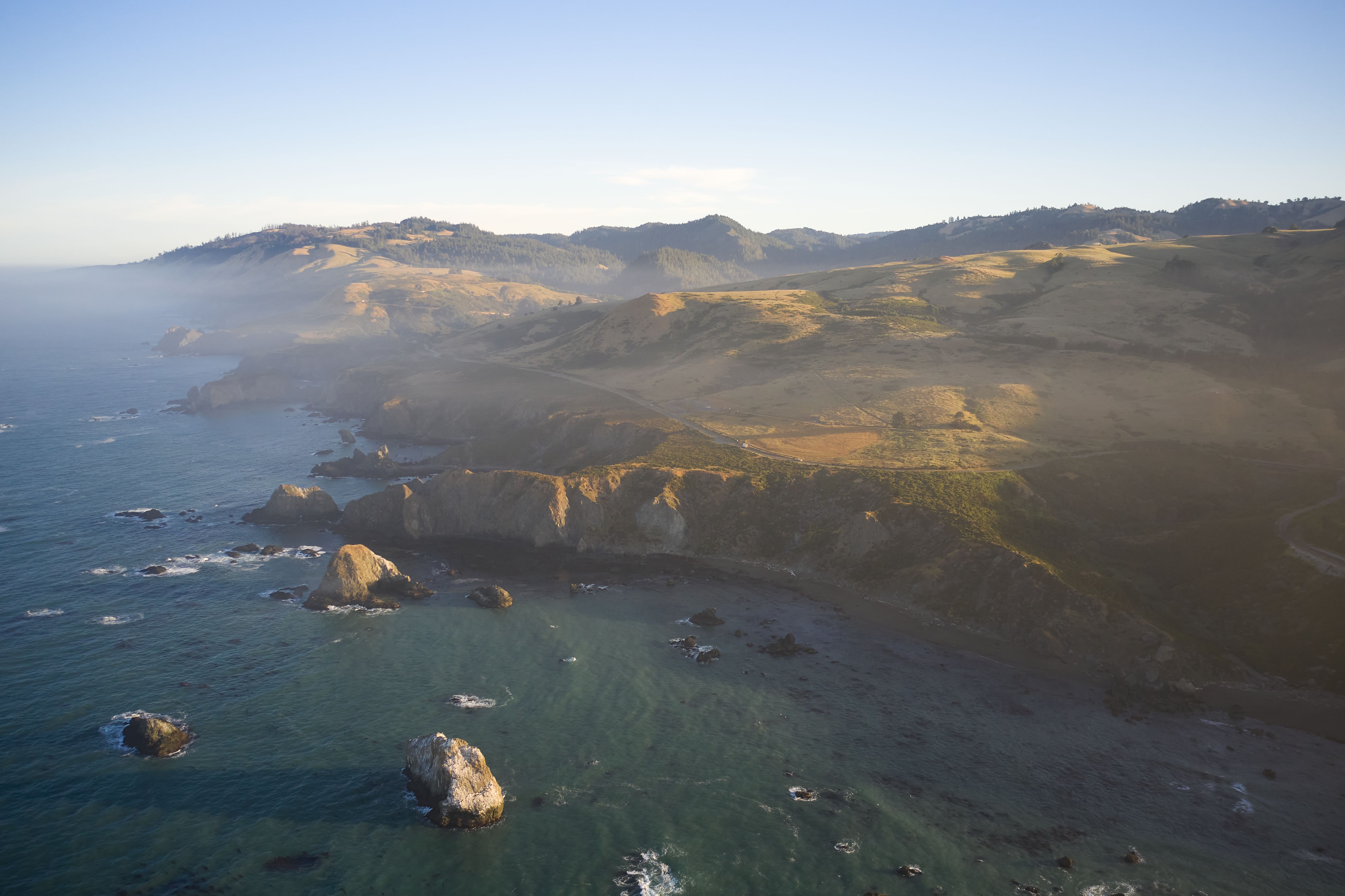 A breathtaking aerial view of Jenner, California's coastline with rocky cliffs and calm ocean at sunset.