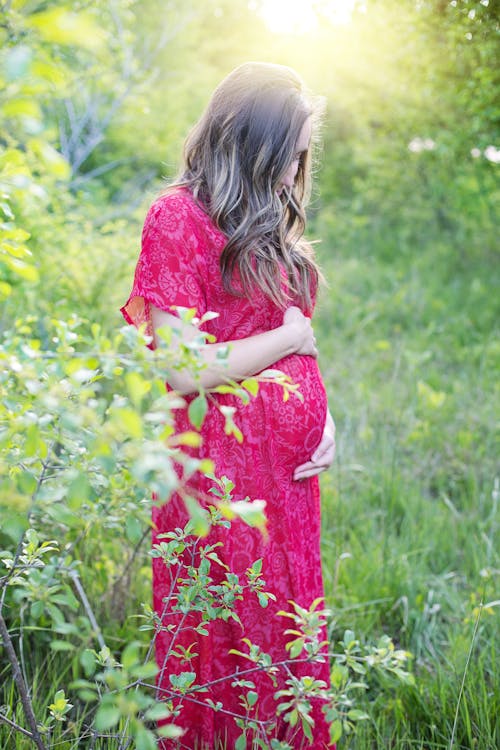 A Pregnant Woman in Long Dress Standing on Green Grass Field