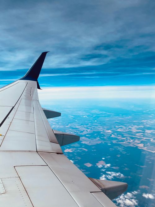 Free A breathtaking view from an airplane window showcasing the wing, blue sky, and white clouds. Stock Photo
