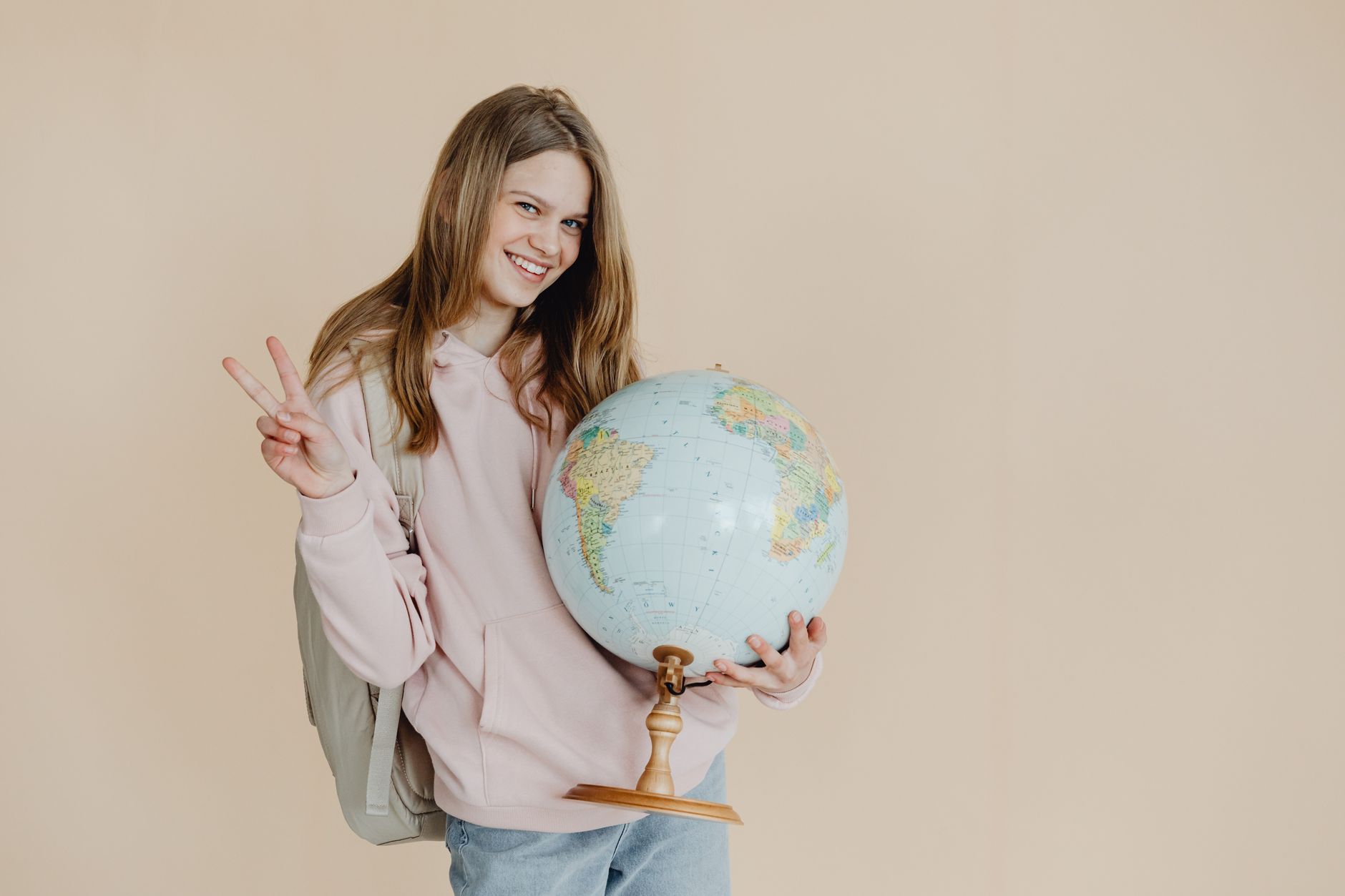 A smiling teenage girl holds a globe, making a peace sign, perfect for back to school themes.