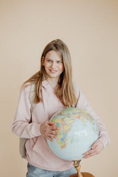 Teen girl in pink hoodie holding a globe, symbolizing education and geography.