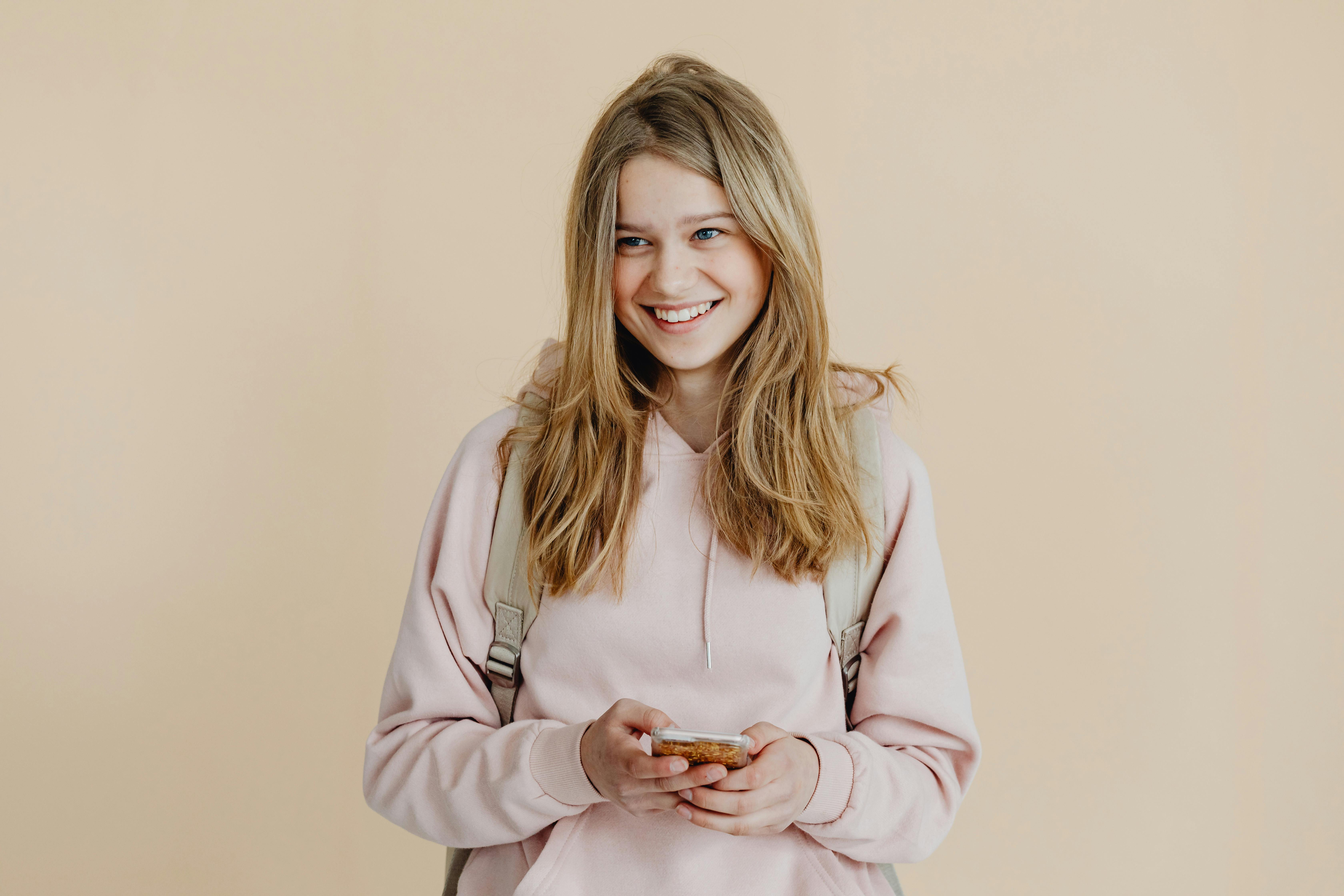 a woman in pink sweater smiling while holding her mobile phone