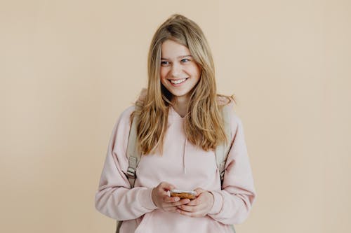 Free A Woman in Pink Sweater Smiling while Holding Her Mobile Phone Stock Photo