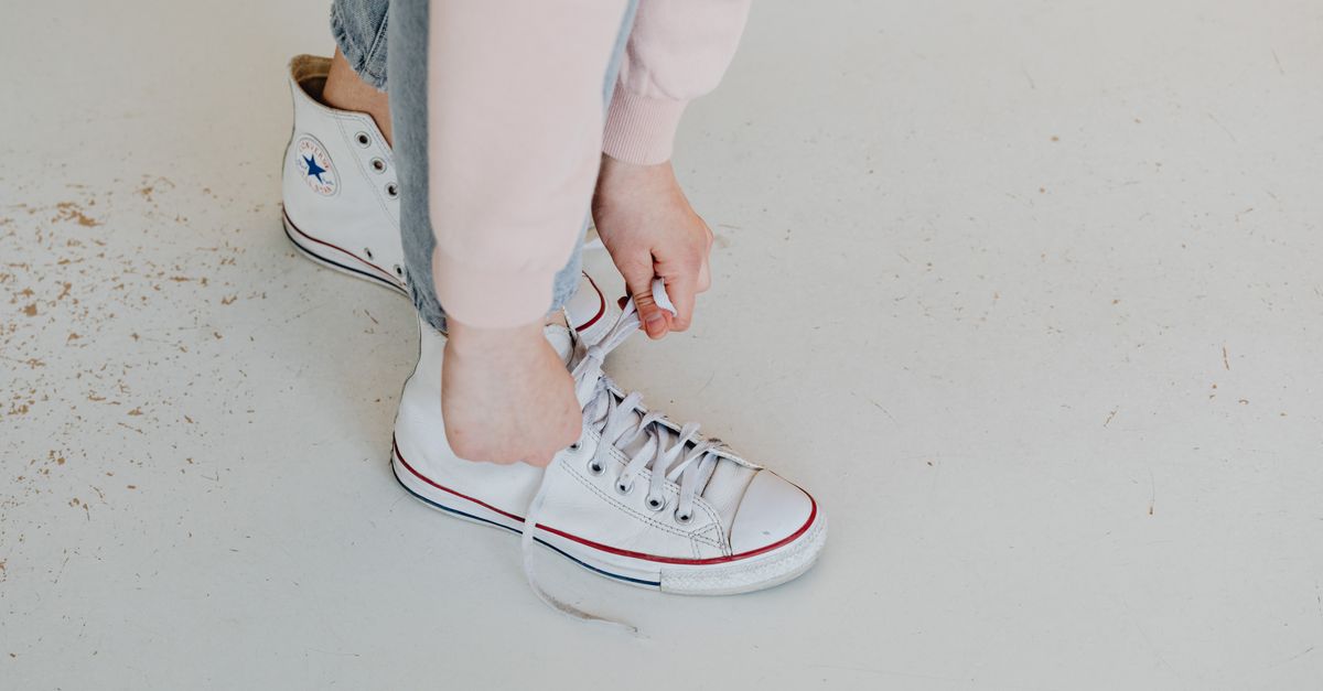Close-up of a person tying white Converse sneakers, captured from above.